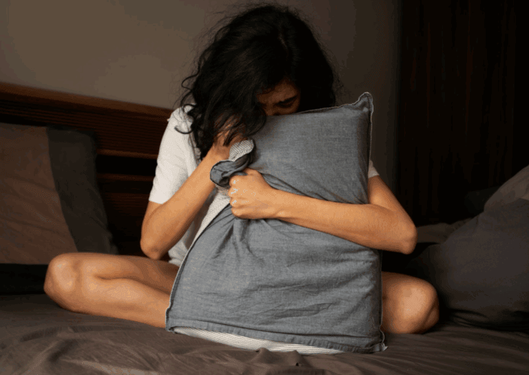 女性因為失眠坐在床上痛苦抱著枕頭。